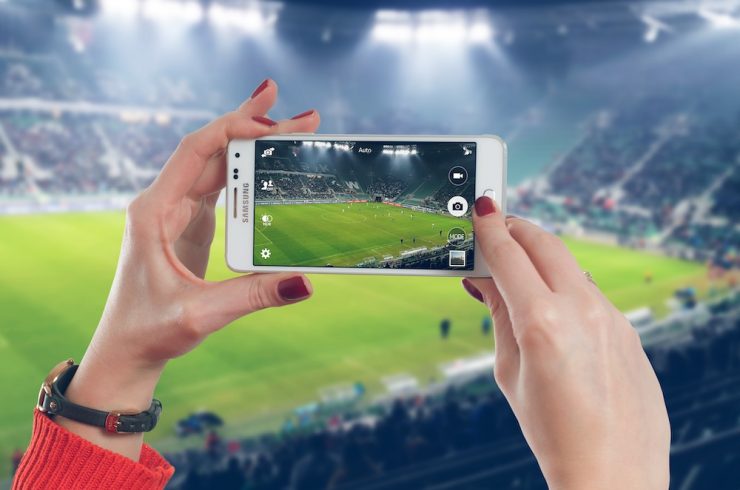 smartphone tenue par une femme prenant la photo d'un stade de football, explicitant la fidélisation dans le sport business